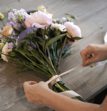 Händer som knyter ett band runt en bukett med blommor på ett träbord.
