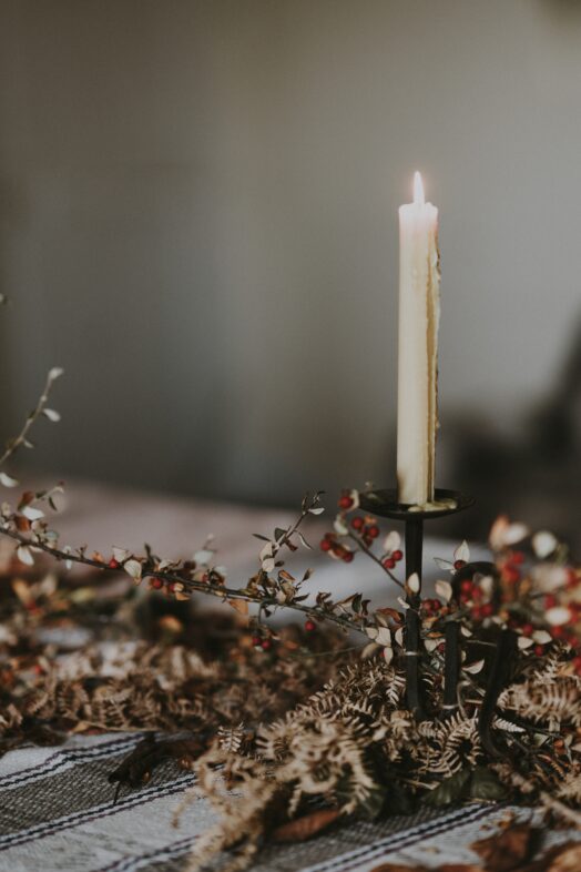 Ett tänt ljus på en ljusstake omgiven av torra blommor.