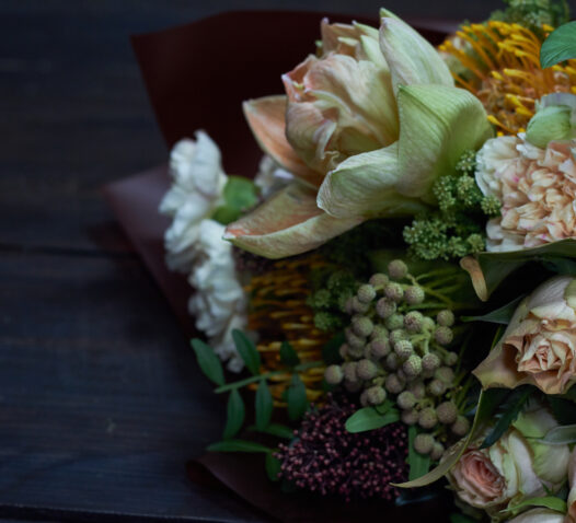 En bukett med olika blommor och gröna blad på ett mörkt bord.